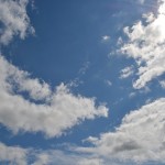 Wolken tegen een blauwe lucht met een zonnetje achter de wolken