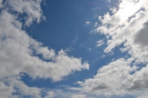 Wolken tegen een blauwe lucht met een zonnetje achter de wolken